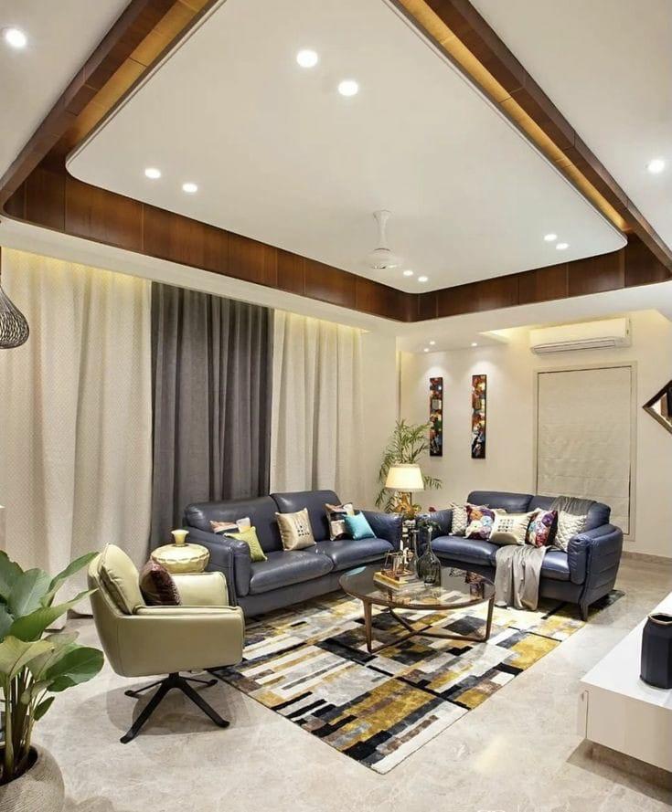 Modern living room featuring dark leather sofas, a geometric rug, and a layered false ceiling with recessed lighting.
