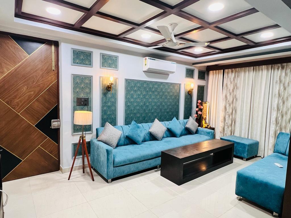 Elegant living room with teal sofas, wooden ceiling design, and decorative wall panels.