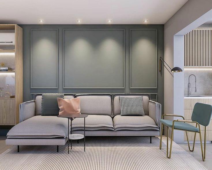 Modern minimalist living room featuring a light gray sectional sofa, sage green wall paneling, and pastel accent pillows.