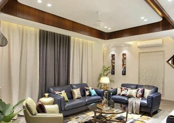Modern living room featuring dark leather sofas, a geometric rug, and a layered false ceiling with recessed lighting.